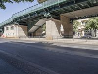 a street in front of a bridge with graffiti on it and cars parked beneath the road