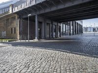 a bridge over a cobbled in brick roadway under a large sky overhead building structure