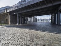 a bridge over a cobbled in brick roadway under a large sky overhead building structure