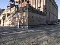 an image of a building with stone and stone stairs and a sculpture on the sidewalk