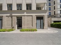 a building has plants in the front of it and bushes on the sidewalk with doors