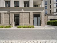 a building has plants in the front of it and bushes on the sidewalk with doors