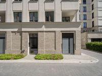 a building has plants in the front of it and bushes on the sidewalk with doors