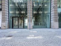 a parked bike is in front of a business building with glass walls and windows that read drive