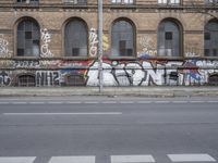 a wall with some graffiti written on it in front of a brick building with arches