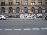 a wall with some graffiti written on it in front of a brick building with arches