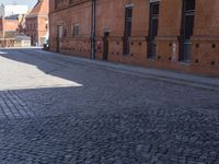 two pink chairs are sitting next to an empty brick walkway, with buildings in the background