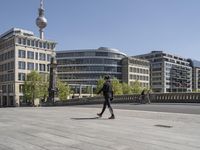 people walking and sitting on a sidewalk in front of some buildings with a television tower