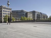 people walking and sitting on a sidewalk in front of some buildings with a television tower