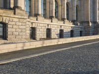 a street with a brick paved road below a big building with pillars and columns around it