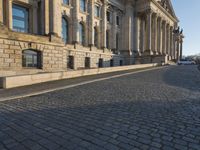 a street with a brick paved road below a big building with pillars and columns around it