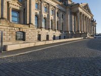a street with a brick paved road below a big building with pillars and columns around it