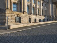 a street with a brick paved road below a big building with pillars and columns around it