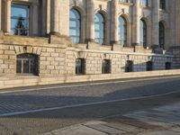 a street with a brick paved road below a big building with pillars and columns around it