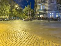 two rows of tables are at the street corner of the city center, in a blurry view of cars on the road