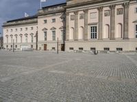 people walking around a stone plaza in front of a large building with a flag on it