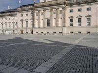 people walking around a stone plaza in front of a large building with a flag on it