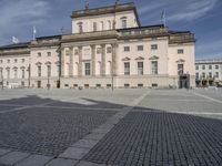 people walking around a stone plaza in front of a large building with a flag on it