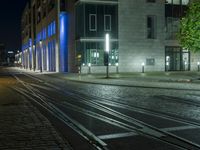 an empty street next to a street light on a rainy night, a train tracks and buildings at the end