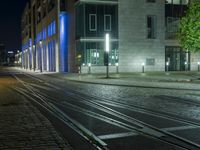 an empty street next to a street light on a rainy night, a train tracks and buildings at the end