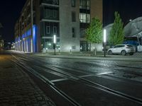an empty street next to a street light on a rainy night, a train tracks and buildings at the end