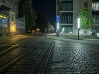 an empty street next to a street light on a rainy night, a train tracks and buildings at the end