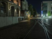 an empty street next to a street light on a rainy night, a train tracks and buildings at the end