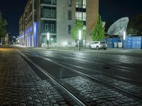 an empty street next to a street light on a rainy night, a train tracks and buildings at the end