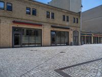 the sidewalk is paved with stones and has a bench in front of it, with no people inside