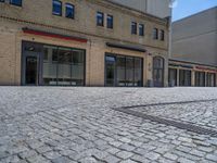 the sidewalk is paved with stones and has a bench in front of it, with no people inside