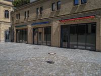 the sidewalk is paved with stones and has a bench in front of it, with no people inside