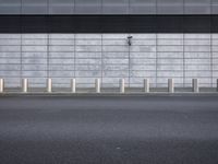 a wall by a street with poles next to it's sidewalk and building wall