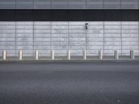 a wall by a street with poles next to it's sidewalk and building wall