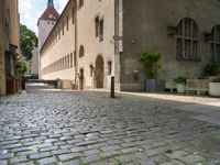 a street with a bench in the middle of the walkway, and a building in the distance