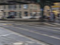 a blurry photo of an intersection with cars and people walking around it and a person on bikes next to a car