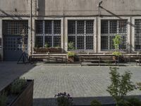 several benches in front of a concrete building with open window panes and potted plants