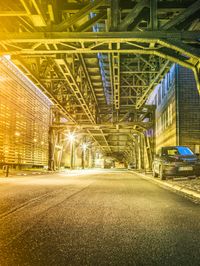 a street under an overpass at night with the lights on and cars parked next to it