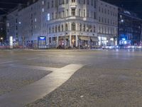 a city intersection has traffic passing by a tall building at night time in europe on a dark stormy day