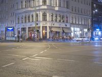 a city intersection has traffic passing by a tall building at night time in europe on a dark stormy day