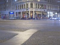 a city intersection has traffic passing by a tall building at night time in europe on a dark stormy day