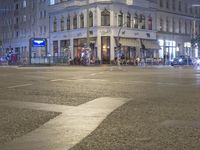 a city intersection has traffic passing by a tall building at night time in europe on a dark stormy day