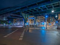 the empty street is filled with people walking and biking under an overpass at night