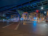 the empty street is filled with people walking and biking under an overpass at night