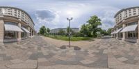 an artistic 360 - pan of a city street with buildings and gardens, with a bench on the sidewalk next to a road