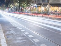 an empty city street with light trails and signs at night, as a man riding his bike walks alongside