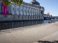 a woman walks next to a large building next to a river, along the waterfront