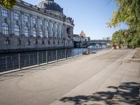 a woman walks next to a large building next to a river, along the waterfront