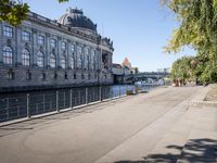 a woman walks next to a large building next to a river, along the waterfront