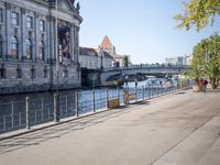 a woman walks next to a large building next to a river, along the waterfront