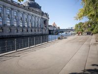 a woman walks next to a large building next to a river, along the waterfront